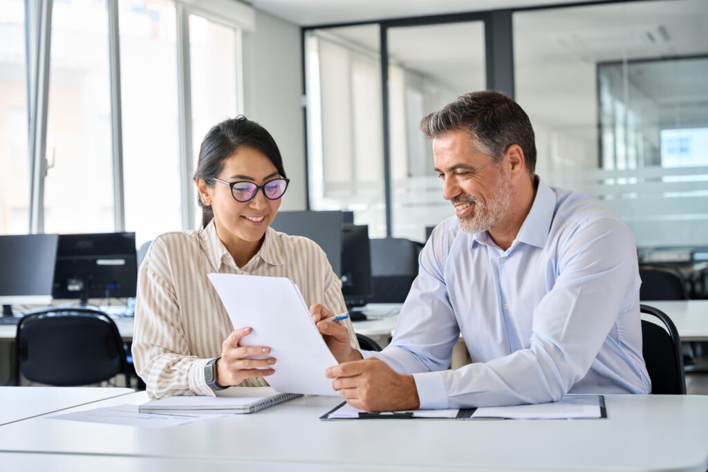 Young Asian account manager advisor lawyer showing paper documents to Latin client partner, diverse professional colleagues discussing tax financial contract papers working in office at meeting.