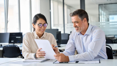 Young Asian account manager advisor lawyer showing paper documents to Latin client partner, diverse professional colleagues discussing tax financial contract papers working in office at meeting.