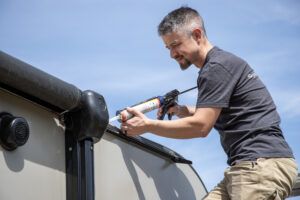A man using caulk on the roof of an RV.