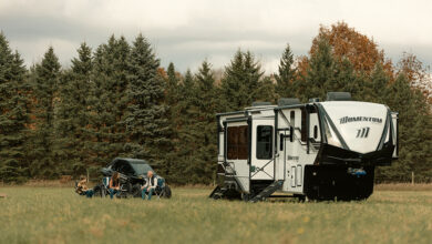 A Grand Design Momentum toy hauler in a field, with a family sitting together outside the RV.