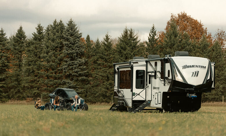 Versatility Built In: Grand Design’s Momentum Toy Hauler 1 A Grand Design Momentum toy hauler in a field, with a family sitting together outside the RV.