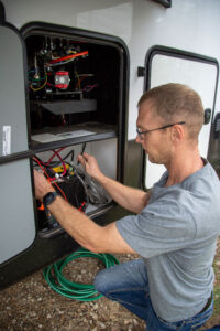 RV technician inspecting and testing electrical components inside an RV compartment.