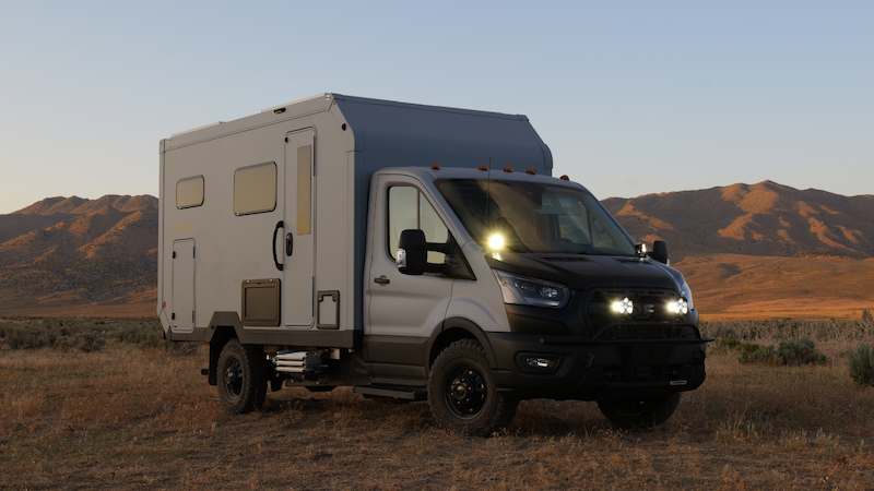 AEONrv To Launch 2025 Model at Overland Expo Pacific Northwest 2 AEONrv off-road RV parked in a desert landscape at sunset, with rugged terrain and mountains in the background.