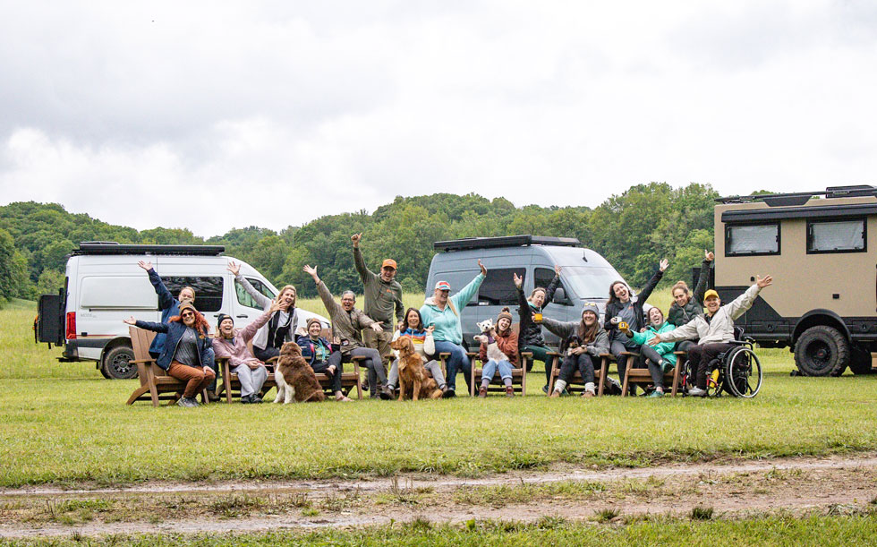A group of people in a field gathered in front of camper vans and RVs to demonstrate fernweh's trips.