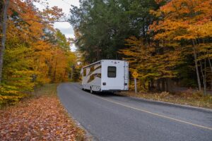 RV driving down a road with fall colored trees lining the roadway on either side.
