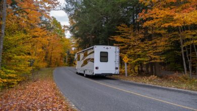 RV driving down a road with fall colored trees lining the roadway on either side.