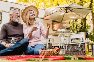 Kiplinger Highlights 10 Reasons To Retire in an RV 2 Aged beautiful caucasian couple having picnic and drinking champagne in the yard near the motorhome.Mature blond lady pointing at something