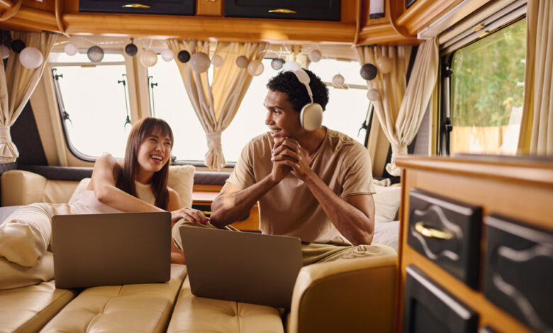 A man and woman sitting in an RV or camper van, with laptops in front of them to demonstrate RV connectivity and Wi-Fi.