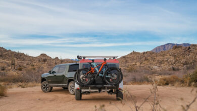 An Escapod teardrop travel trailer being pulled by a pickup truck off-road in a desert.