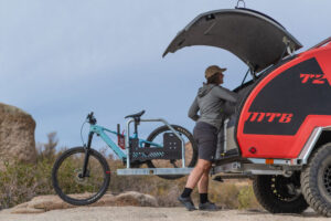 Small but Mighty: Escapod’s Off-Road Teardrop Camper 2 The back of a red Escapod teardrop camper with a woman accessing the hatchback and a blue bike standing next to the camper.