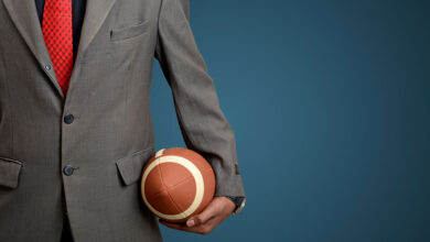 A man in a suit holding a football against a blue background, to illustrate using fantasy football tactics.