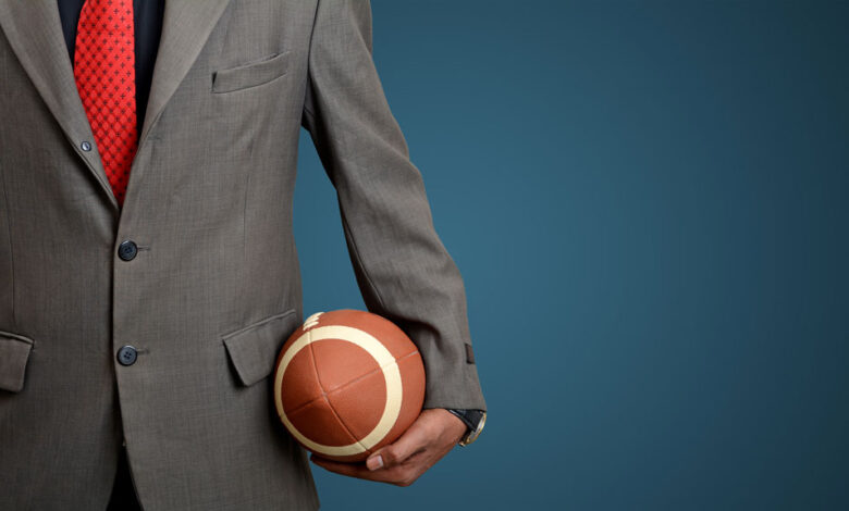 4 Fantasy Football-Inspired PR Tips To Grow Your Business 2 A man in a suit holding a football against a blue background, to illustrate using fantasy football tactics.