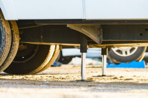 Auto leveling system for camper. Hydraulic steady leg in use. Blue leveler ramp chock block for rv in background.