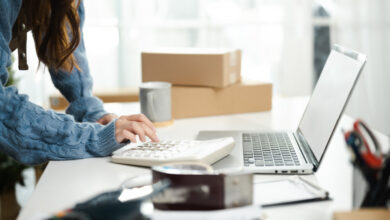 A woman with a calculator and laptop to demonstrate managing your RV parts and accessories department inventory.