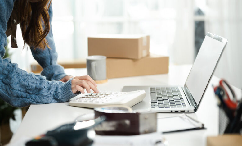 A woman with a calculator and laptop to demonstrate managing your RV parts and accessories department inventory.
