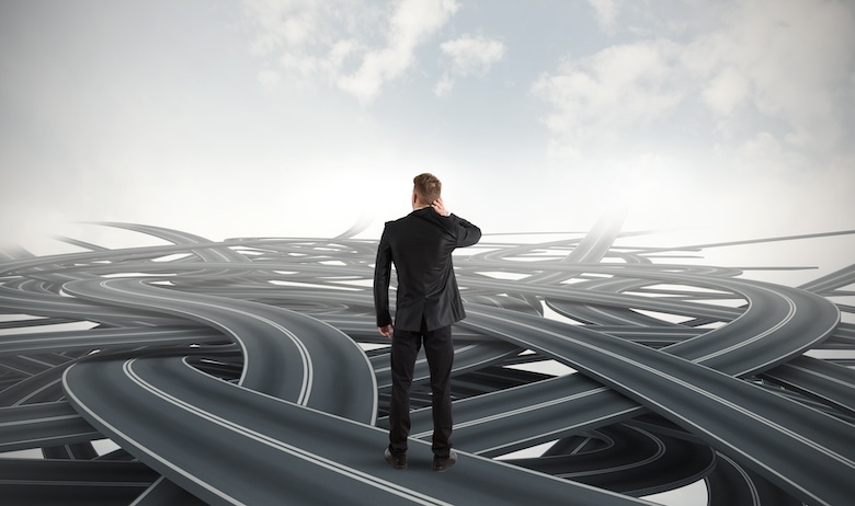 A businessman facing many winding roads, illustrating the difficulty of making leadership decisions during a crisis.
