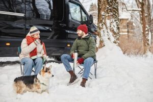 28M Americans To Go RVing This Winter 2 Full length portrait of happy young couple travelling by van in winter forest and sitting outdoors with a Corgi.