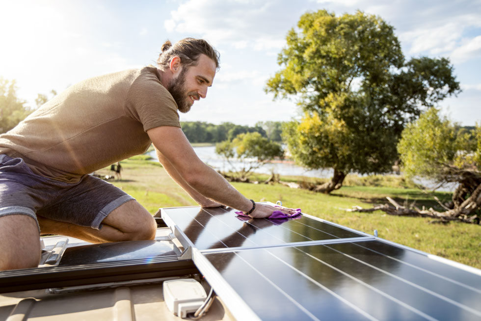 man cleaning the solar panel on the roof of a camper van