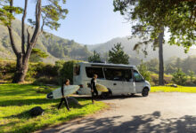 A Leisure Travel Vans RV in the wilderness, with two people carrying surfboards walking away from the RV.