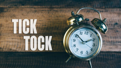 An analog clock lying on a wooden background next to the words 'Tick Tock' to indicate the need for urgency and speed when it comes to repair event cycle time (RECT) at RV dealerships.