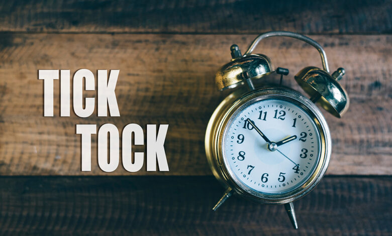 An analog clock lying on a wooden background next to the words 'Tick Tock' to indicate the need for urgency and speed when it comes to repair event cycle time (RECT) at RV dealerships.