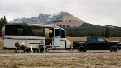 An image of Lightship's EV RV AE.1 being towed by a black pickup truck, with a couple camping outside the travel trailer.