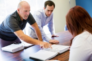 Optimize Your RV Dealership During Peak Season 3 Bald man points to small print during a meeting while his colleague reads along, demonstrating taking care of customers during peak season.