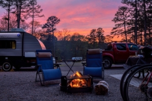 RoverPass 2026 Report: Outdoor Hospitality’s Historic "Quality Shift" 2 Two chairs around a fire pit with a truck hauling a travel trailer RV behind it, with a beautiful pink sunset in the background.