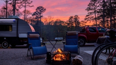 Two chairs around a fire pit with a truck hauling a travel trailer RV behind it, with a beautiful pink sunset in the background.