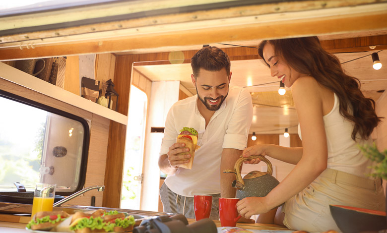 Happy young couple having breakfast in trailer view from outside. Camping vacationUntitled