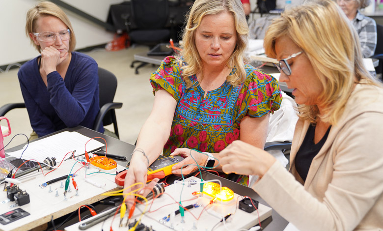 Women sit around a table with wired technical schematics, illustrating women's technical training for the RV industry.