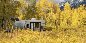 Travel trailer parking among yellow bushes and aspen trees during fall foliage with snowcapped mountain behind. Camping in golden autumn scenery at Gunnison National Forest in Colorado, USA