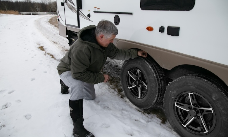 A man kneeling next to an RV, demonstrating the need to inspect RV tires for UV and ozone damage.